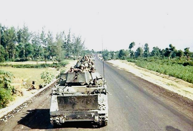 H Troop armored cavalry vehicles traveling along a paved road through the Vietnamese countryside