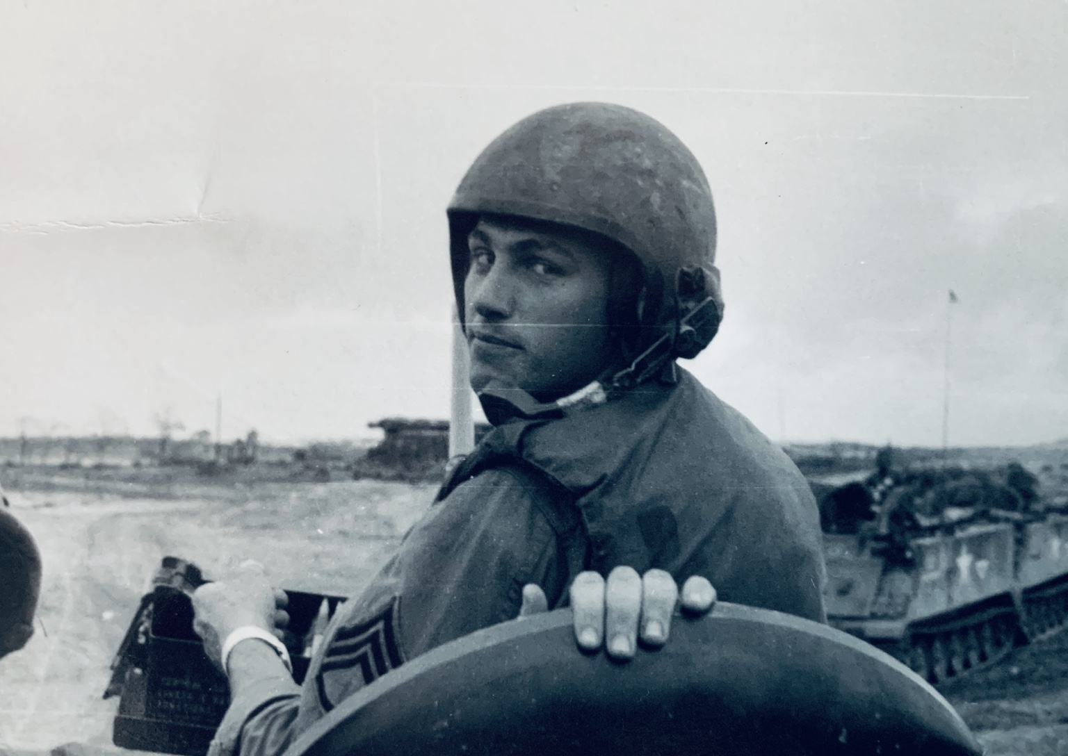 A helmeted trooper looking toward the camera from an armored vehicle, with another track behind him. Name, date, and location remain unidentified.