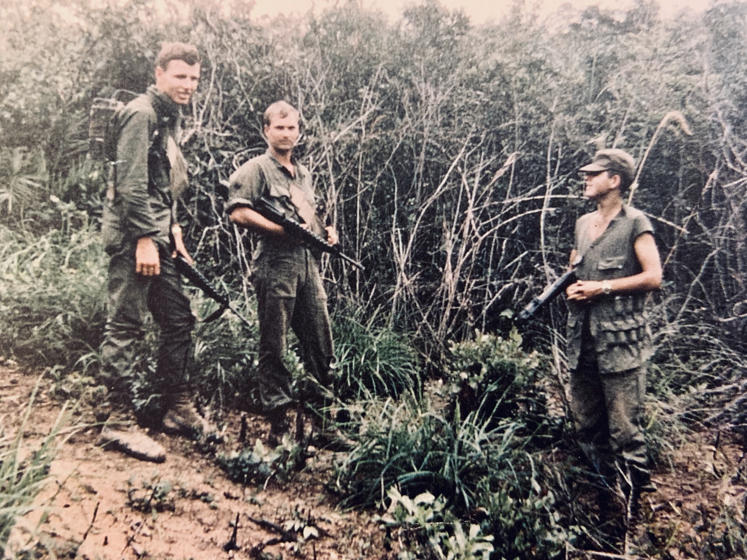Three troopers with their equipment beside dense brush. Names, date, and location remain unidentified.