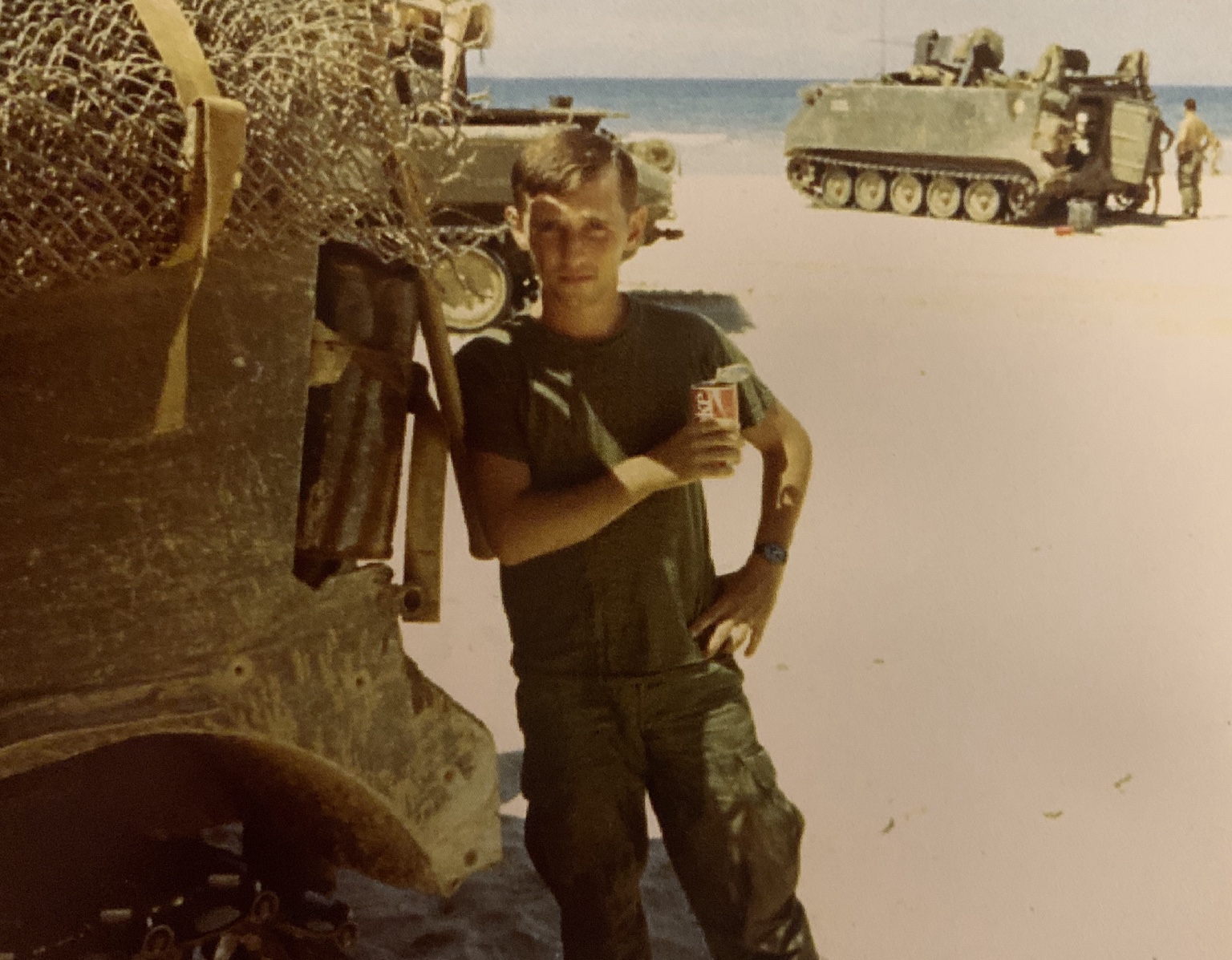 A trooper holding a beverage can beside a track, with additional tracks near a shoreline behind him.