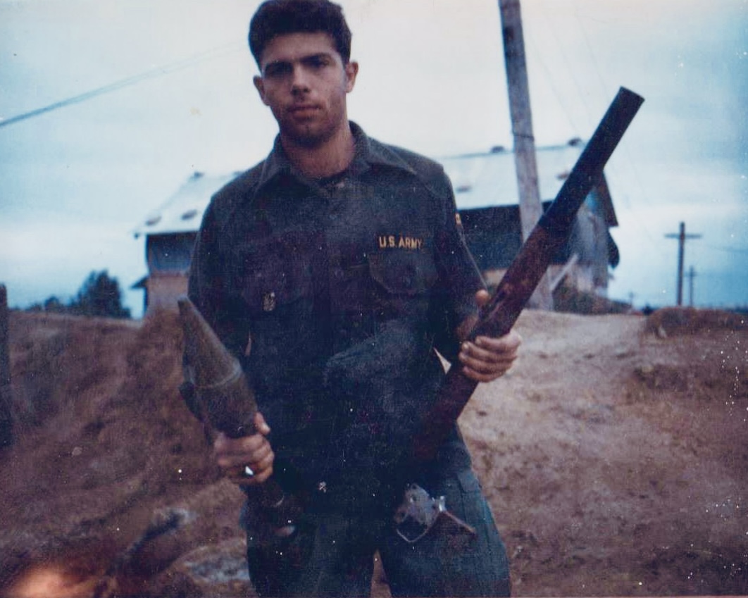 A trooper holding a rifle near base buildings. Name, date, and location remain unidentified.