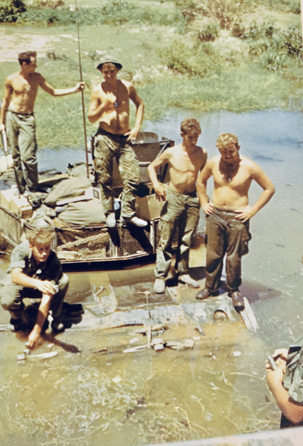Five troopers standing or sitting aboard a mud-covered track in shallow water.